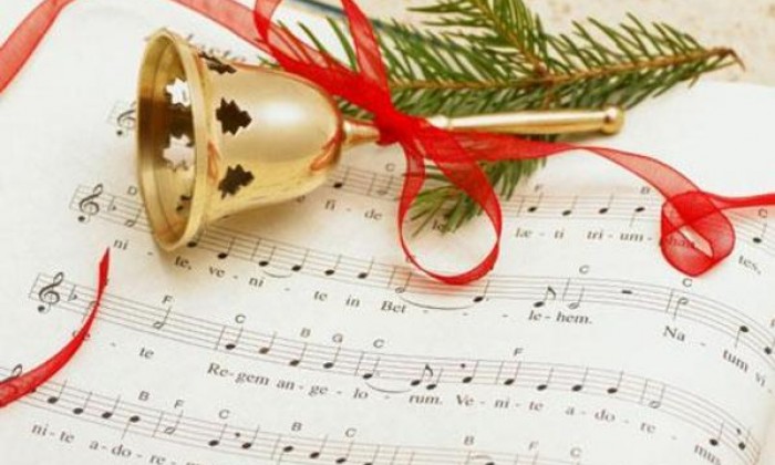 Sheet music with a bell, red ribbon and piece of pine tree on top
